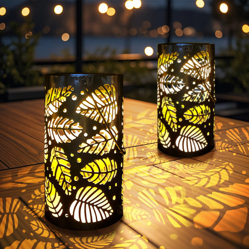 Deux lanternes solaires en métal ajouré à motif feuilles posées sur une table