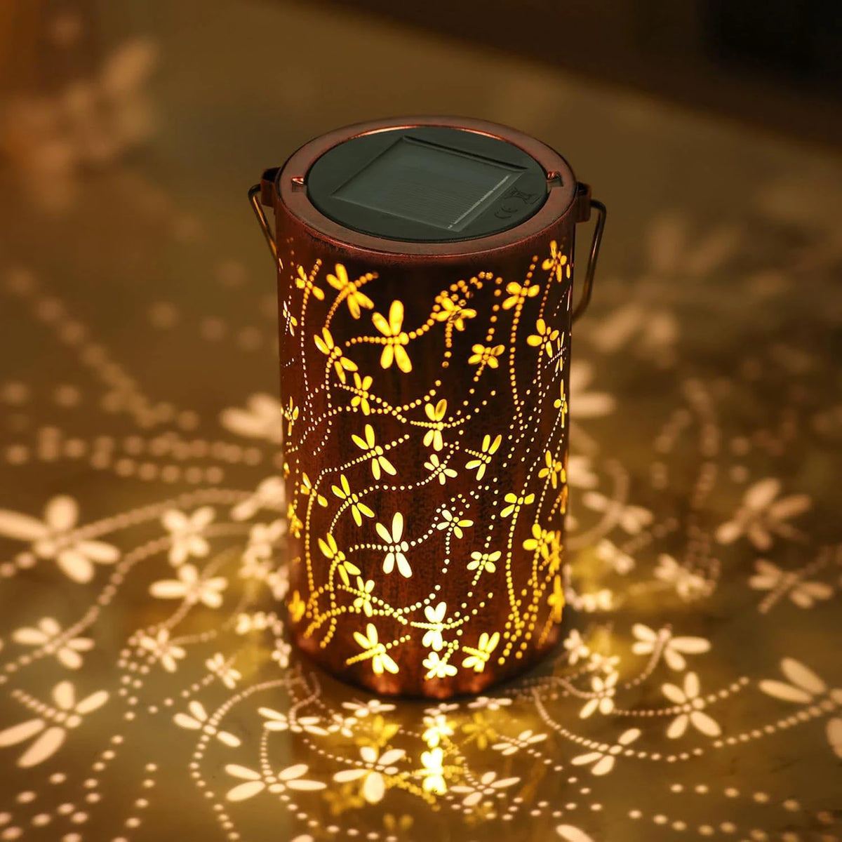 Lanterne solaire en métal ajouré à motif libellule projetant une lumière décorative